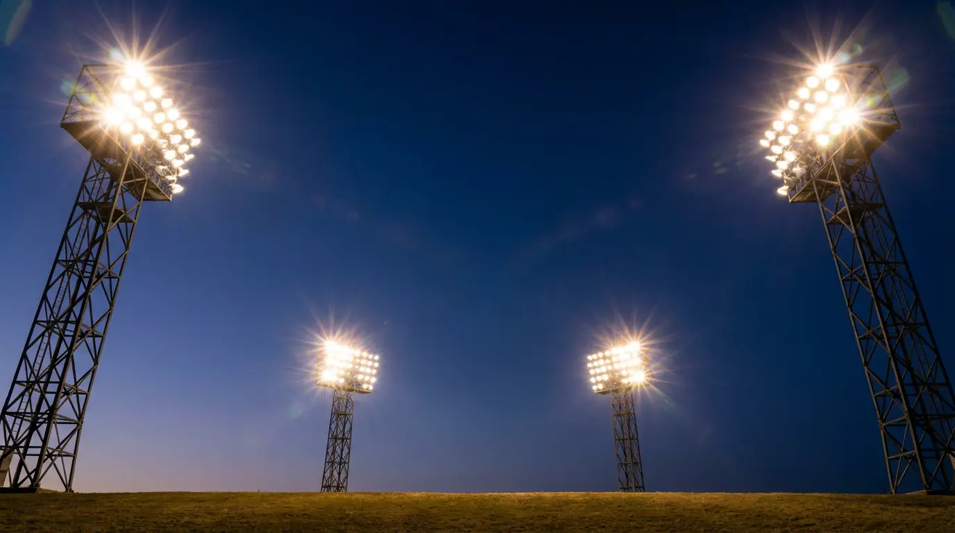 Jalkapallostadionin valotornit palamassa kirkkaasti tummaa iltataivasta vasten